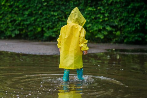 Jonge jongen met laarzen speelt in een tuin die overstroomd is door regenwater, symbool voor risico op waterschade in Rotterdam.